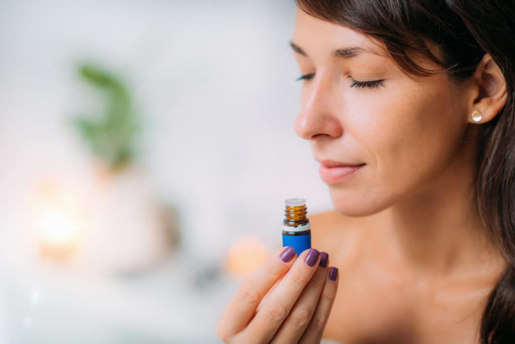 Holding and Smelling Ayurvedic Oil woman holding open bottle of essential oil under her nose to inhale the aromatherapy oil for congestion