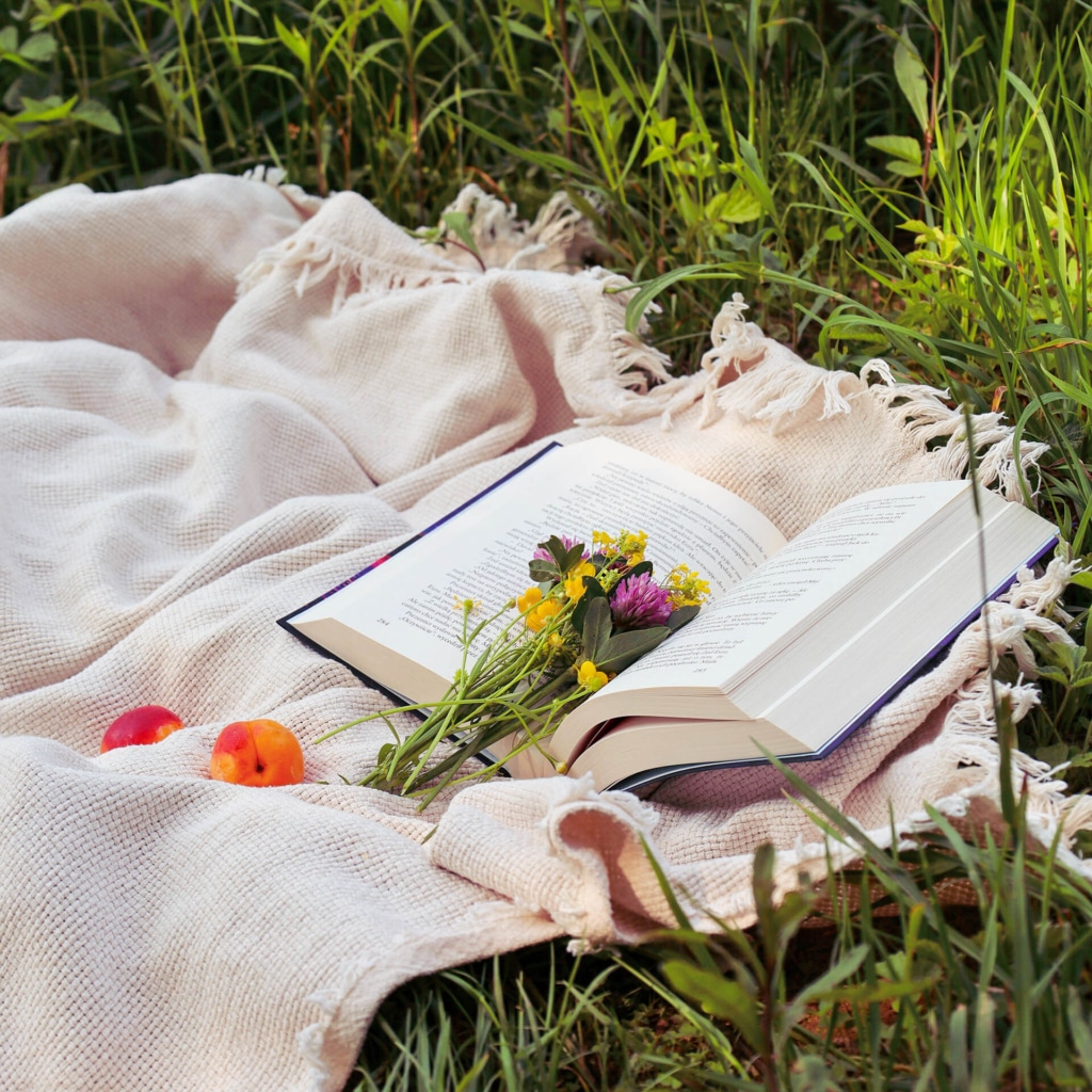 Herb Book herbalism and aromatherapy book open laying on a blanket in grass with fresh flowers resting on top